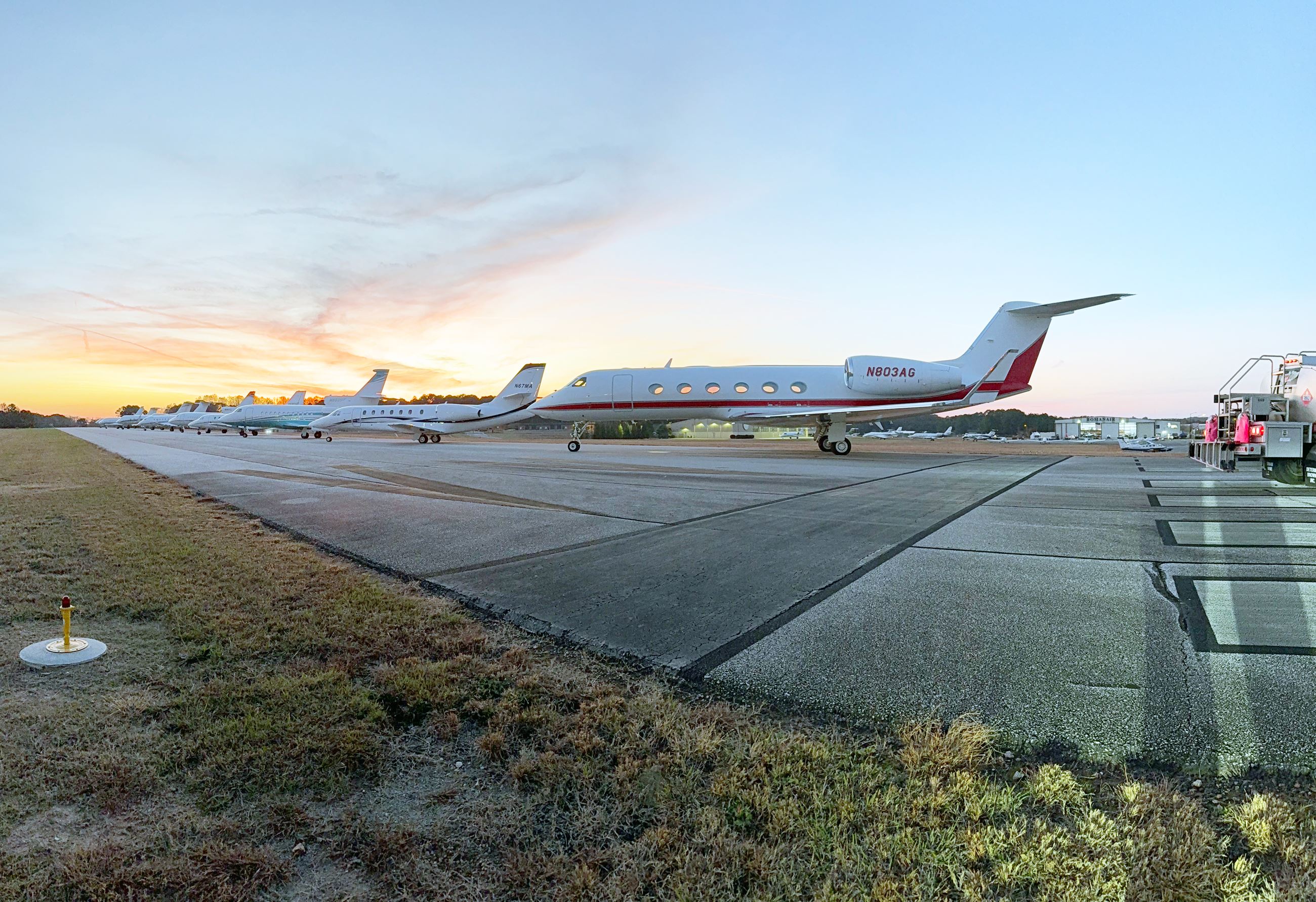A row of airplanes is shown parked along a runway at the Barrow County Airport.
